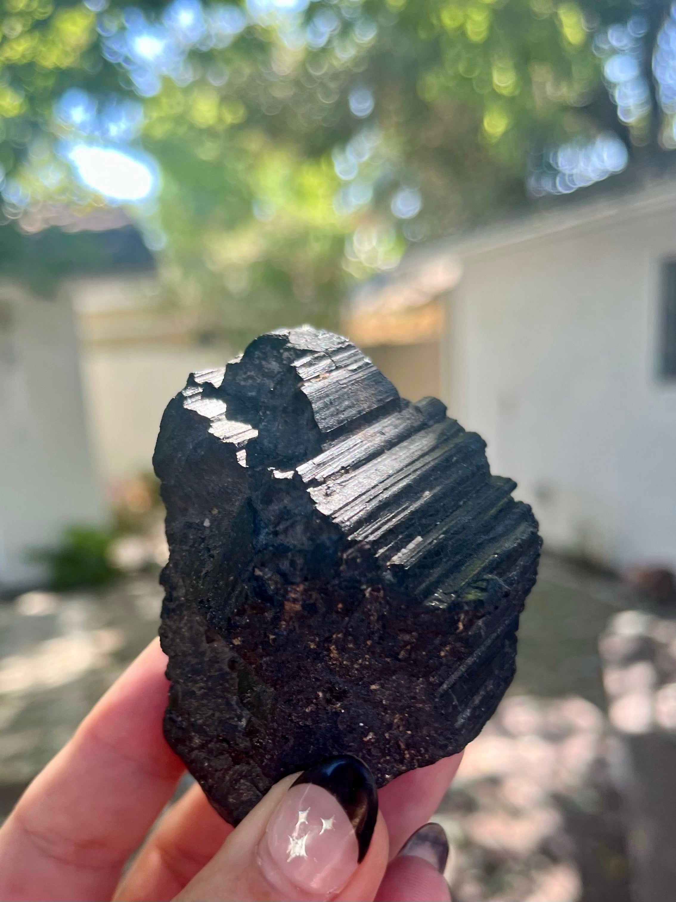 Black tourmaline protection crystal displayed by female hand outdoors in nature