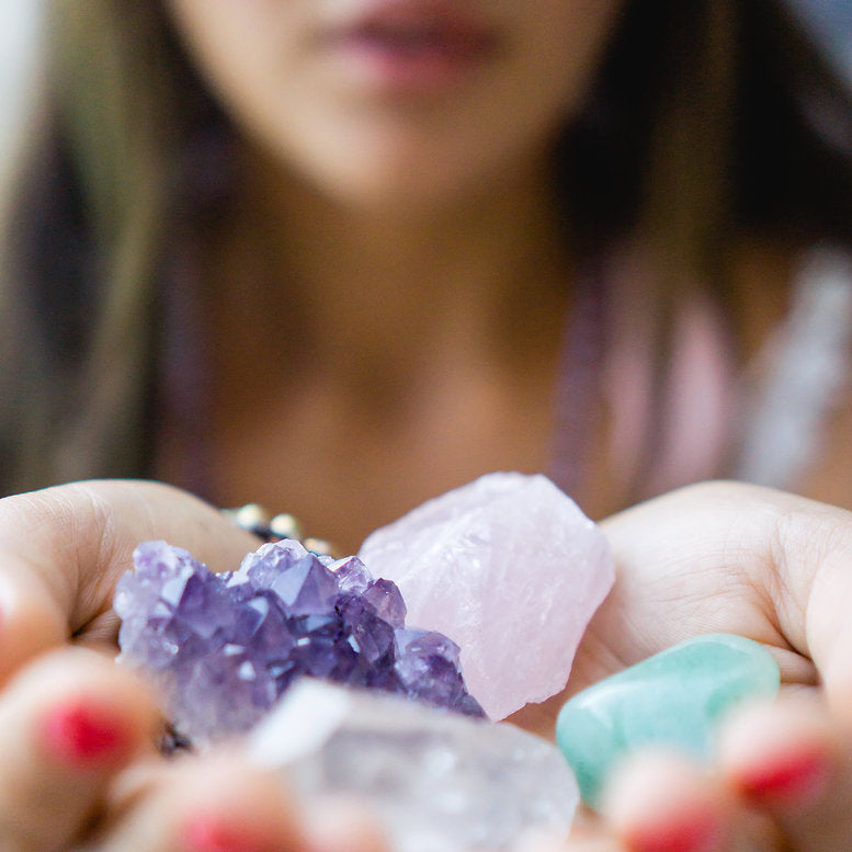 Young woman using both hands to hold healing crystals out in front of her - amethyst, rose quartz, clear quartz point, and green aventurine.