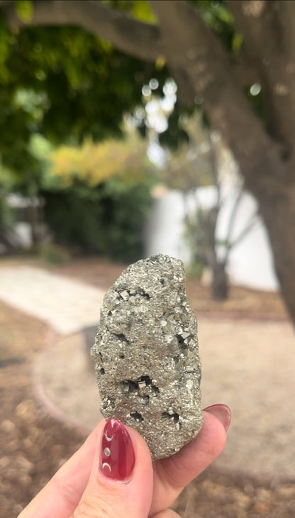 Pyrite raw crystal wealth stone held in female hand in nature