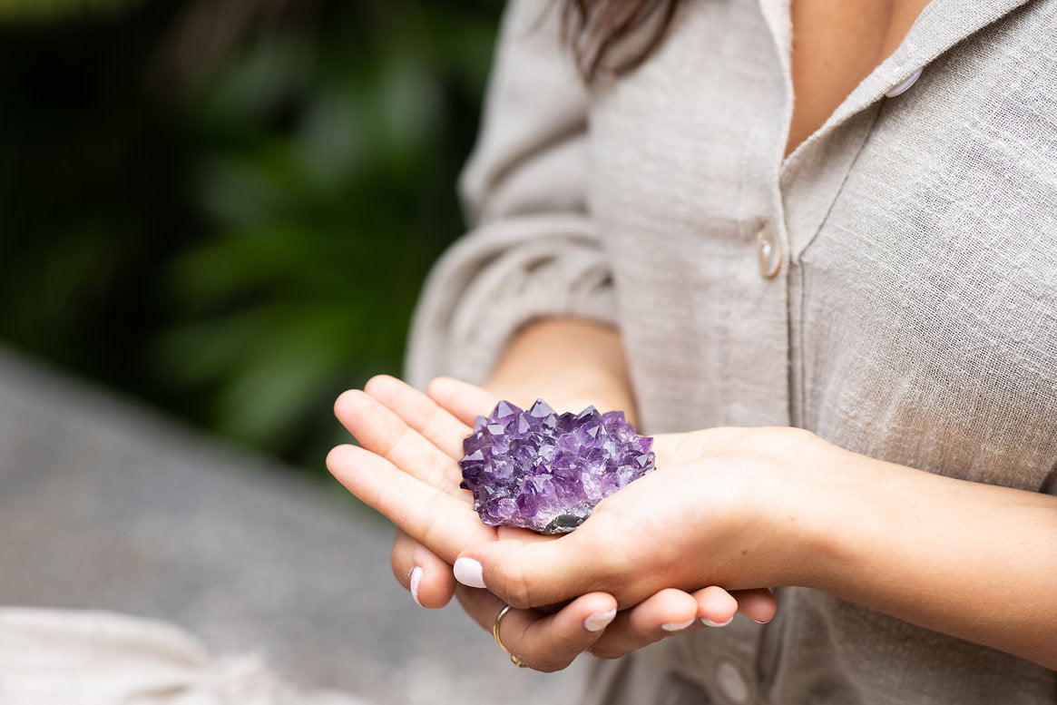 Women holding a raw amethyst crystal cluster in her hands near her heart.